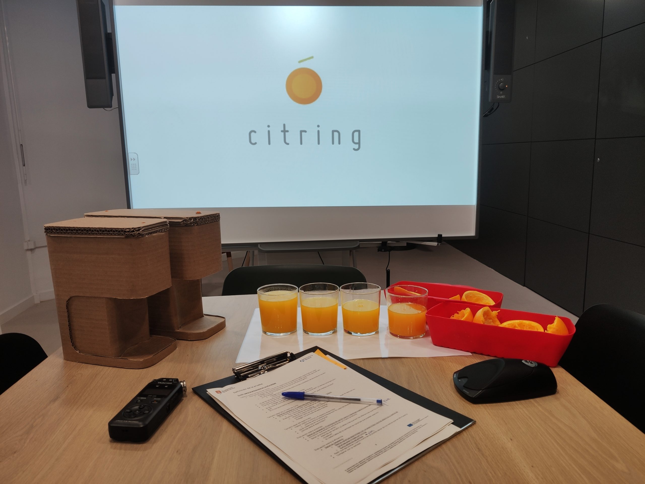 Image shows, two prototypes, a screen, 4 orange juices, orange pieces, a recorder and script